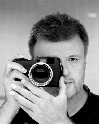 Freelance photographer holding rangefinder camera to his eye.